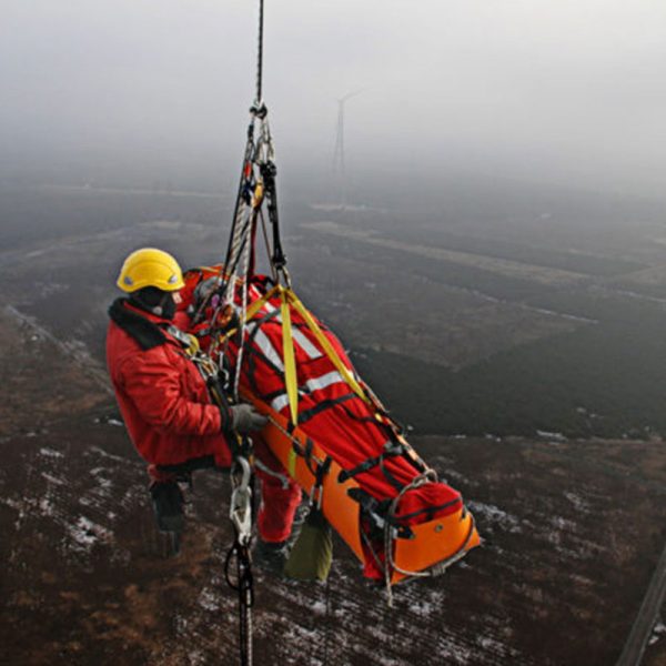 A man in a Sked® Basic Rescue System – International Orange jacket is hanging from a helicopter.