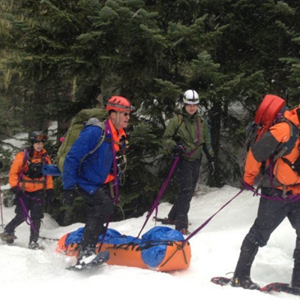 A group of people carrying a Sked® Stretcher – International Orange – Stretcher Body Only up a snowy slope.