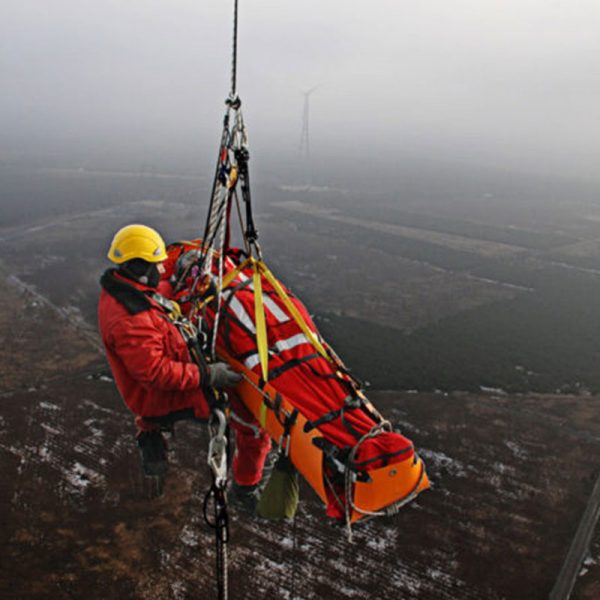 A man in a Sked® Stretcher – International Orange – Stretcher Body Only jacket is hanging from a rope.