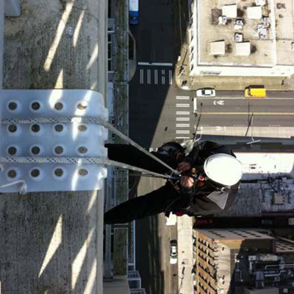 A man is hanging from a ledge of a building, using the Rope Tracker.